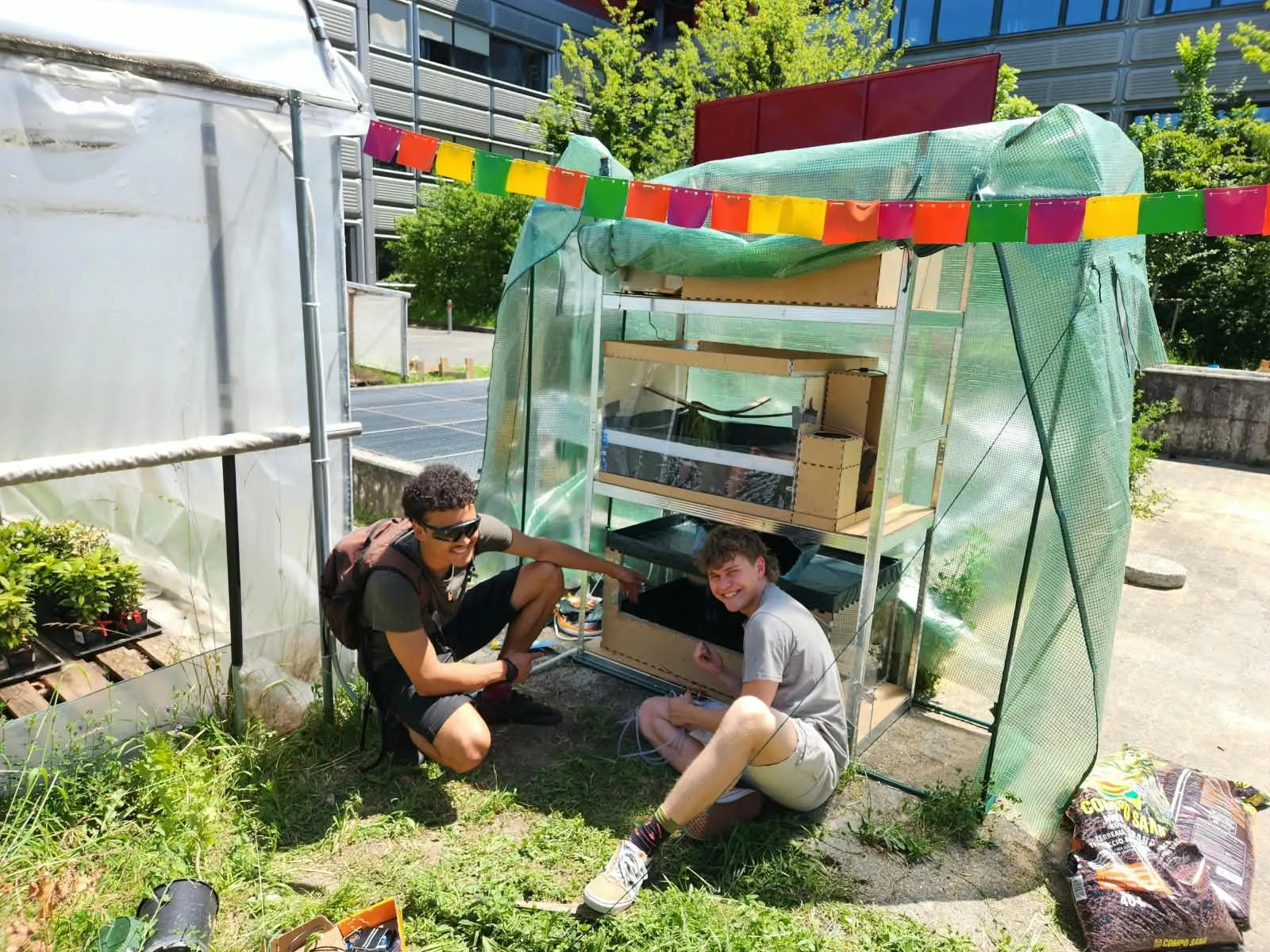 Two Carbon Team members smiling while building a prototype inside a small greenhouse on campus