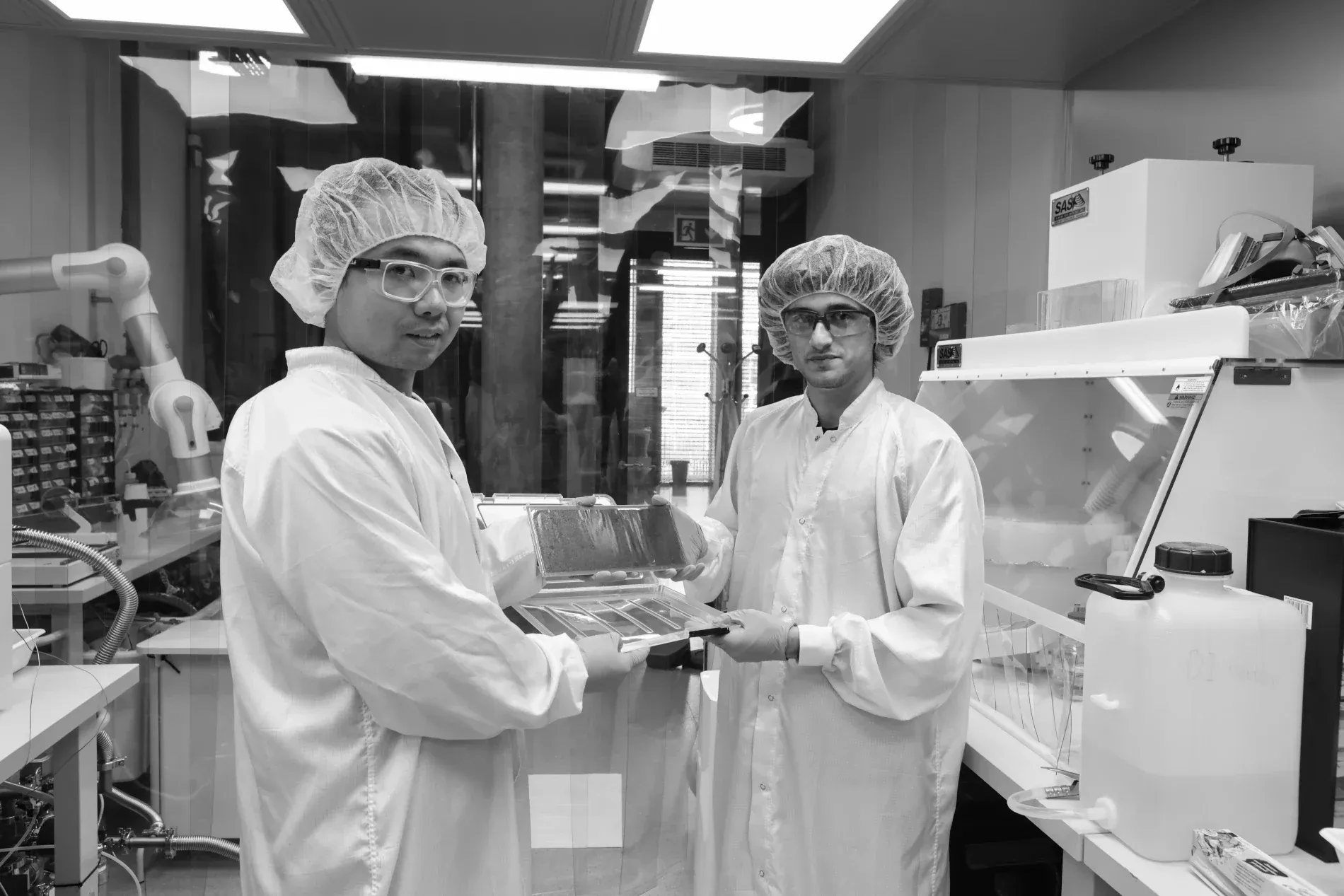 Two students in clean-room suits handling membrane samples in a lab